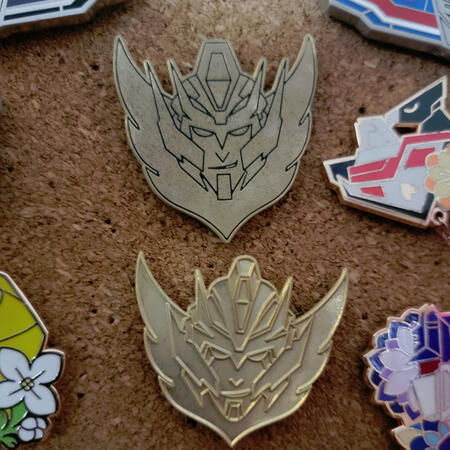 Two gold enamel pins, produced several years apart with different styles.